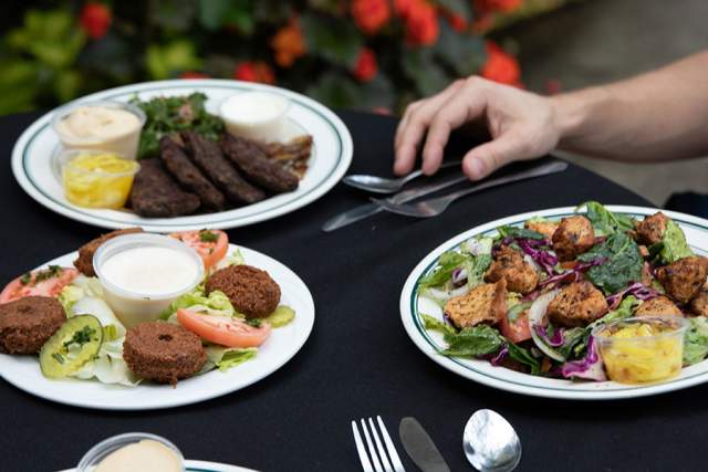 Table of three plates of food with a person reaching for silverware