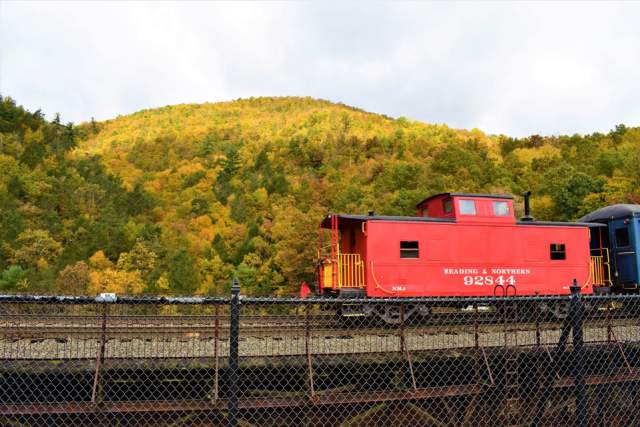 A red train car sitting on railroad tracks in front of fall foliage filled trees