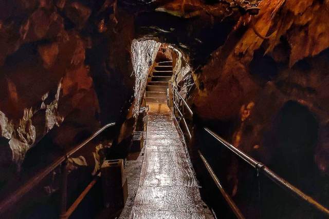 Pathway inside a dark cavern with a light at the end of the path leading to a stairway.