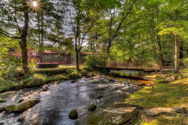 Exterior of a green cabin with a stream running in front of it and a bridge to cross