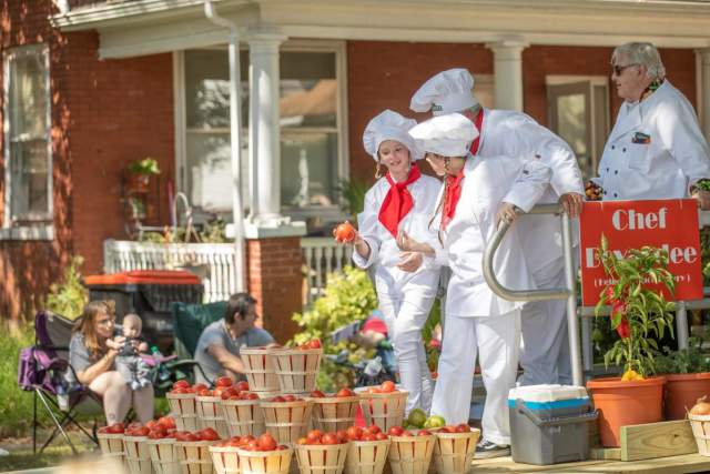 Three kids dressed in chef uniforms with large chef hats and a red scarf standing over buckets of apples