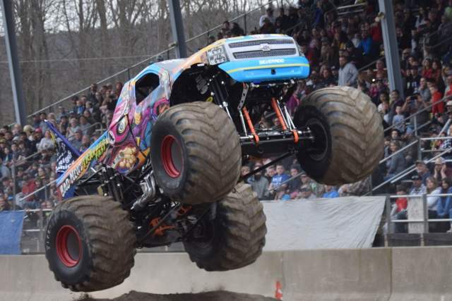 A monster truck jumps over an obstacle in front of a crowd