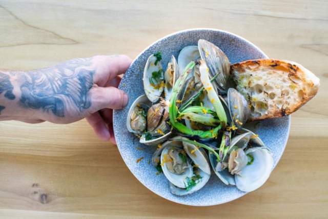 A hand holding a bowl of sea food shells served with a piece of bread