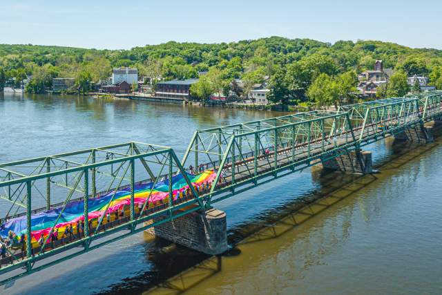 A crowd carrying a large rainbow flag across a bridge