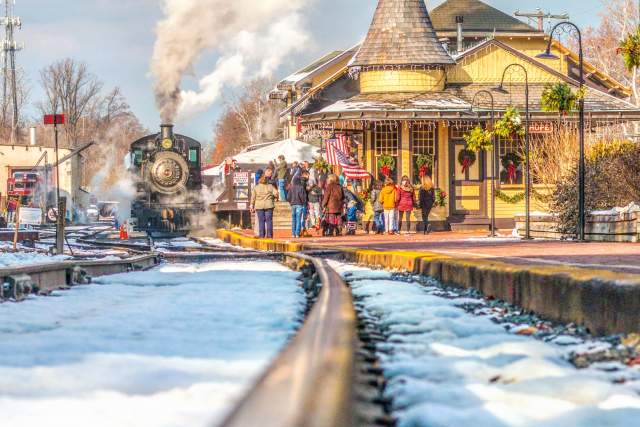 Close up of train tracks with the New Hope Railroad train blowing smoke and people getting on the train in the distance.