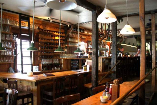 A moody, empty bar with shelves of liquor, low bar lamps over the counter, and bar seats