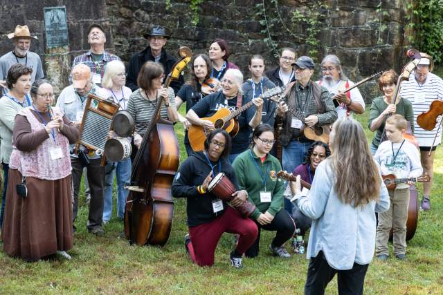 Group of people playing all different instruments in an outdoor grassy area