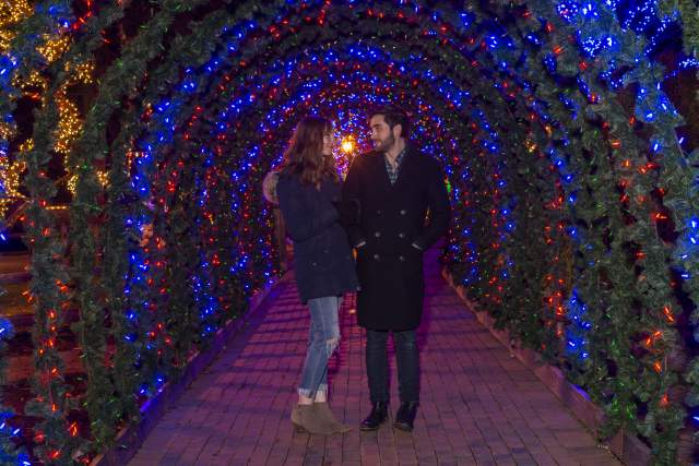 A man and woman walking arm and arm through an arch of holiday lights