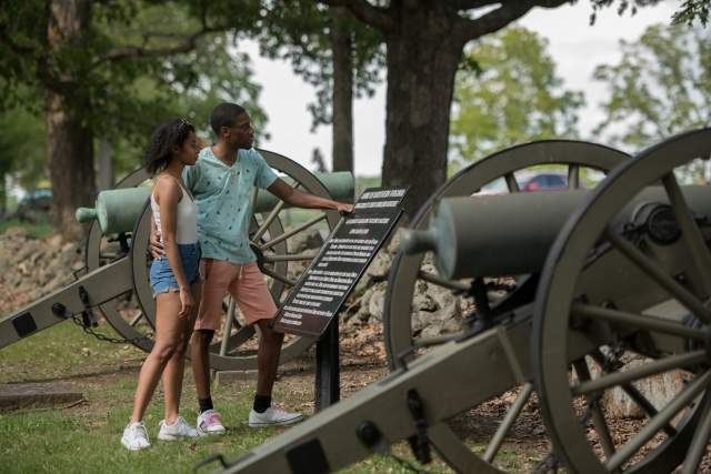 A man and woman reading a plaque that stands next to old canons
