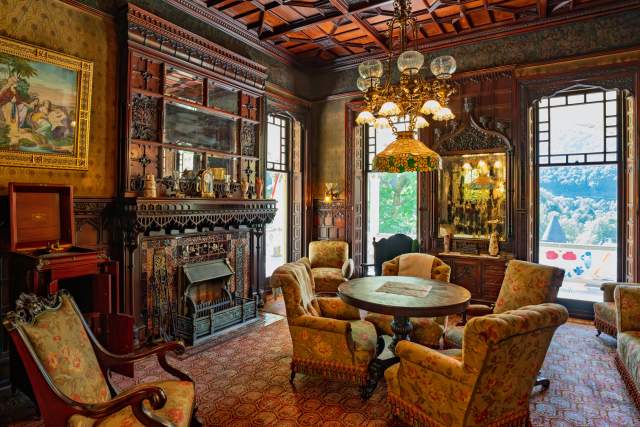 Interior of an old, historical, Victorian era mansion living room with chairs around a table, a luxurious fireplace and a chandelier