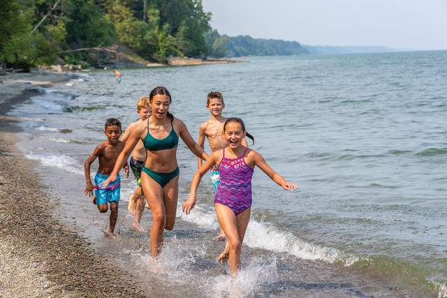 Five kids in bathing suits running through small waves in the water on the beach