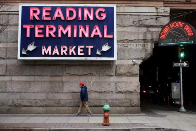 Person walking on a sidewalk in front of a sign that reads Reading Terminal Market