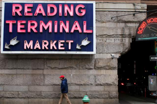 Person walking on a sidewalk in front of a sign that reads Reading Terminal Market