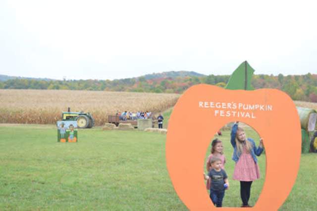 Three kids standing in an enlarged pumpkin cut out posing for a photo on a farm