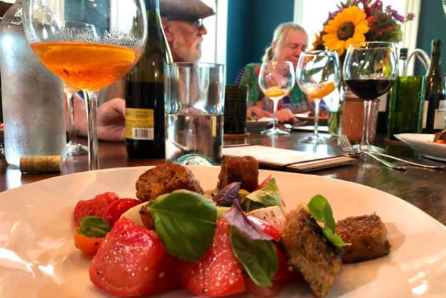 A plated salad with a glass of wine sitting to the side on a table with a group of people eating