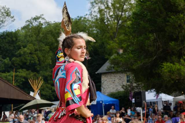 A woman in Native American headdress and attire dancing in front of a crowd