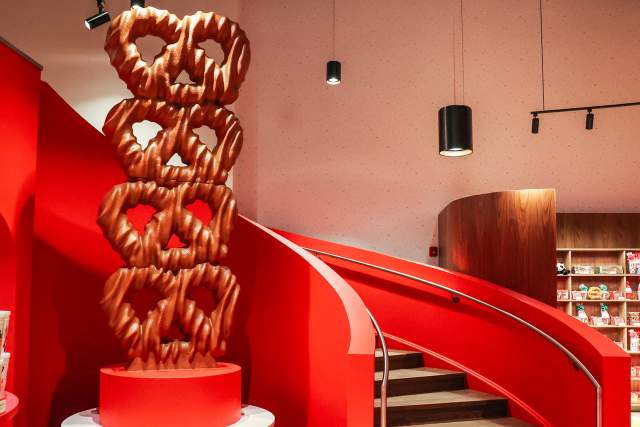 Interior of a colorful candy store with a sculpture of four pretzels stacked on one another standing next to a winding staircase