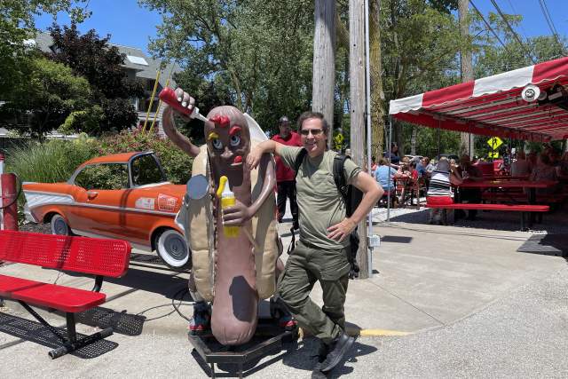 A man leaning up against a hotdog statue