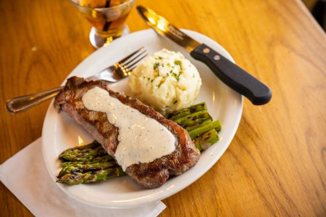 Aerial of a plated dinner with a piece of steak with hollandaise sauce set on asparagus with a side of mashed potatoes.