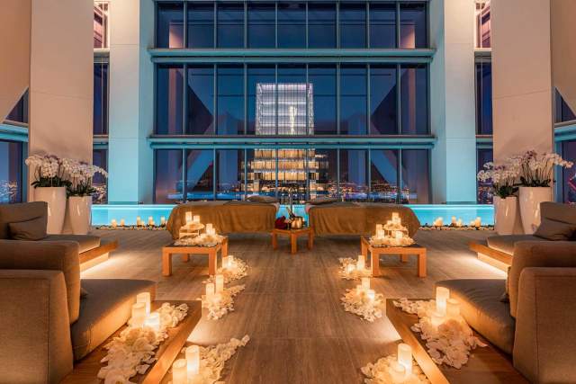 Spa area decorated with lit candles, two massage tables, and beautiful ambiance in front of a floor to ceiling window