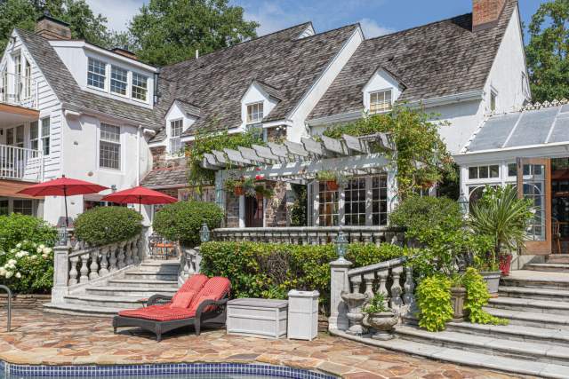 Exterior of the backyard mansion on a sunny day  with a porch and stairs leading to a pool
