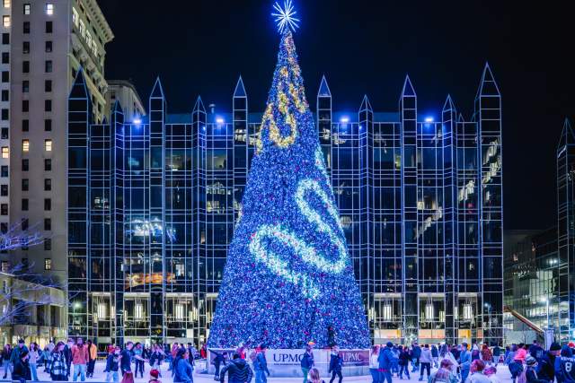Large decorated glowing Christmas tree overlooking people ice skating on an outdoor ice skating rink in Pittsburgh
