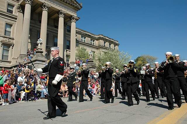 Men in uniform marching down a street with people watching