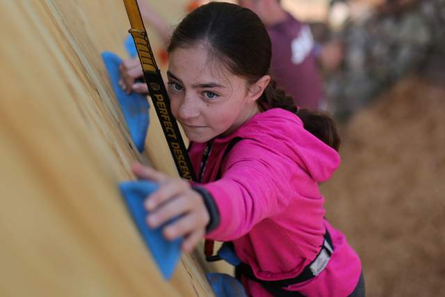 Young girl climbing up a rock climbing wall