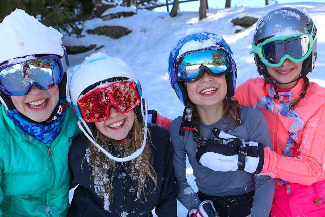Four kids in snow gear on a snowy mountain posing for a photo
