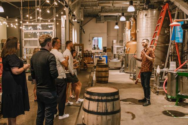 People on a tour at an indoor distillery listening to a guide