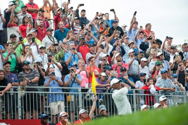 People in stand watching a person hit a golf ball with a club