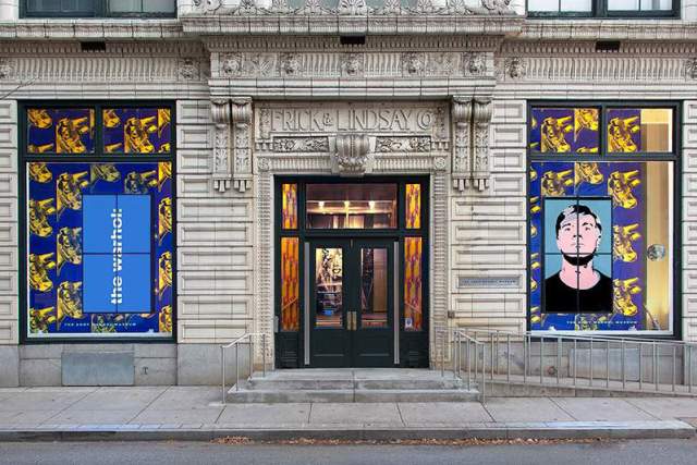 Andy Warhol museum entrance with a front door and two large windows showcasing art work posters.