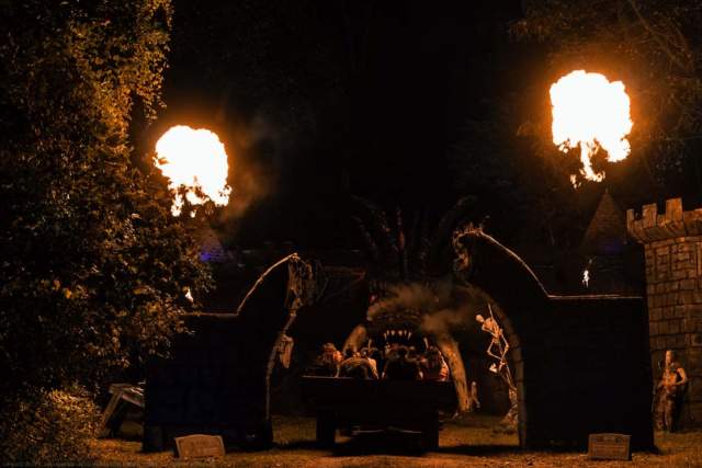 Hayride going through an archway at night. Two fire torches are lit on either side of the archway to light the way.
