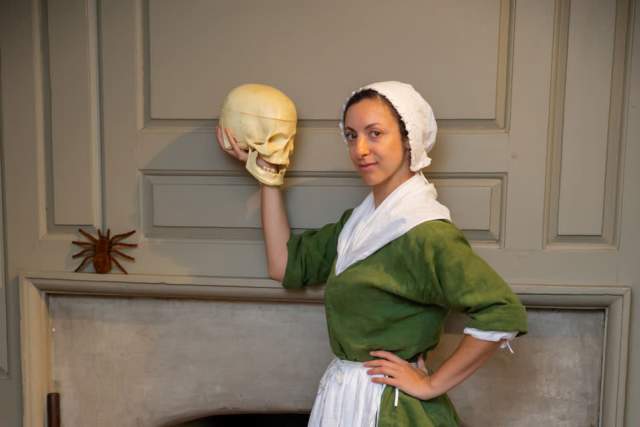Colonial woman holding a skull in front of a fireplace