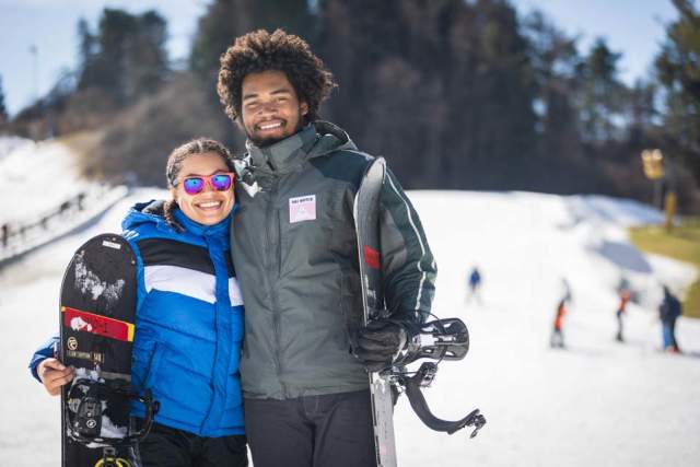 Couple posing with snowboards with a snow covered ski slope in the background