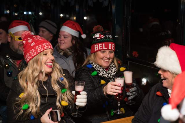 Three women in Santa hats cheersing glasses of champagne while sitting on a BYOB Holiday Lights Trolley