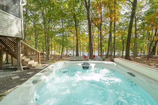 A person in a hot tub in the woods looking out at a lake