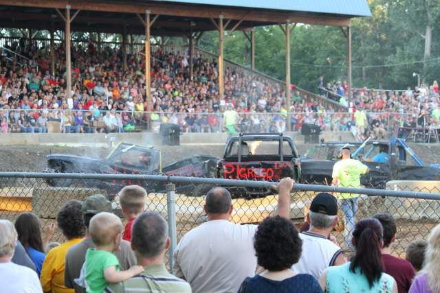 A stadium of people watching cars crash into one another in dirt arena