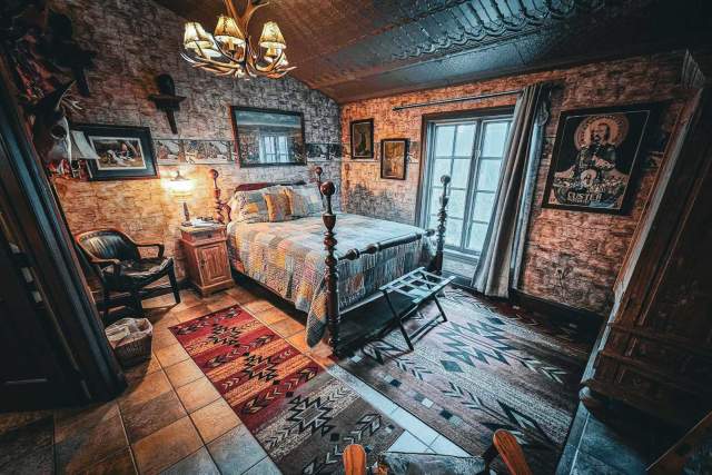 A creepy room inside Farnsworth House in Gettysburg with a full bed with plaid bedding, vintage photographs, and a chandelier light made out of antlers