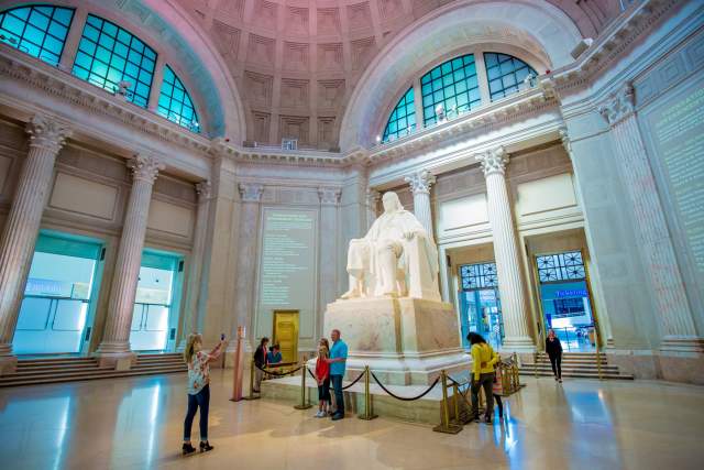 Interior of the Franklin Institute in Philadelphia with an enlarged statue of Benjamin Franklin and people pose to take pictures in front of it.