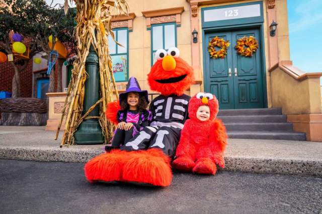 Person in an Elmo costume sitting on a front step with two small children