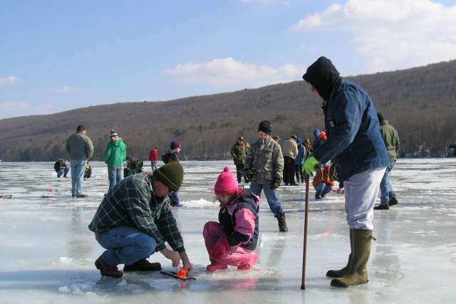 Adults and children ice fishing on a frozen lake