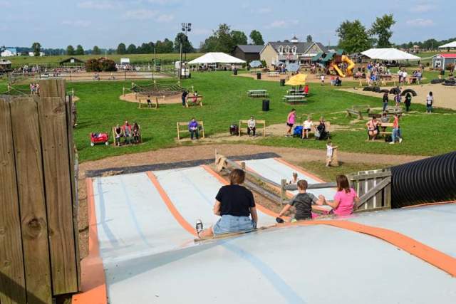 An adult and two kids sliding down a large outdoor slide at a farm