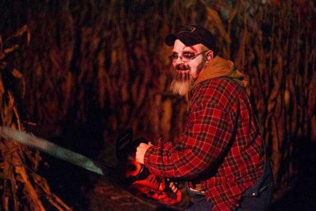 A man with white face paint holding a chainsaw in front of a cornfield in Lancaster