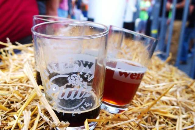 Three half drank glasses of beer sitting on a hay bail