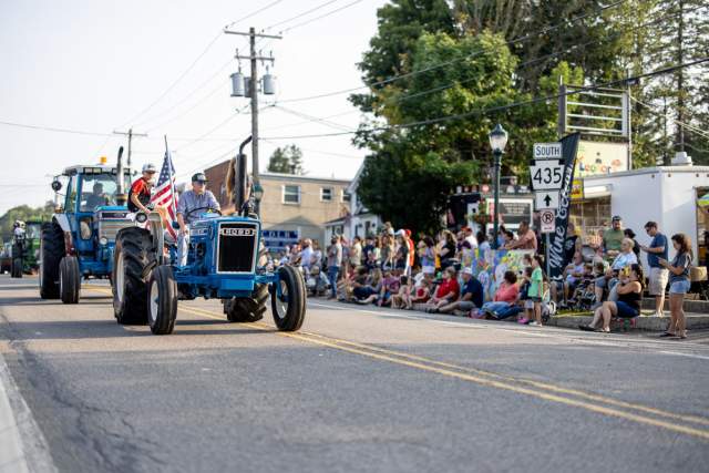 Tractors in a street parade with a crowd of people watching