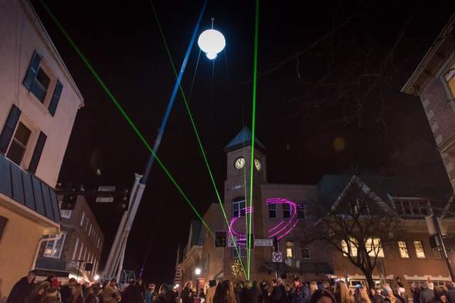A glowing mushroom being dropped by a crane at night for a New Year's Eve celebration in the Kennett Square town center with people looking up