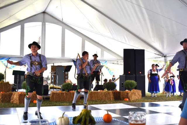 Men dressed in German Oktoberfest attire dancing in front of a band