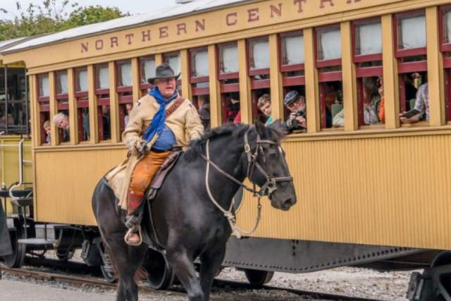 Man riding a black horse next to adults and children on a train