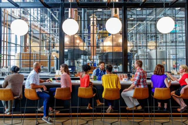 People sitting at a bar being served at a distillery.